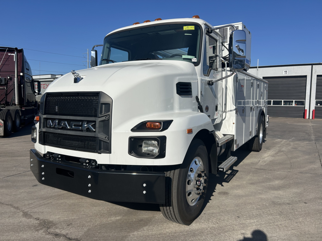 White 2025 Mack MD7 service truck front-left view showing bold grille with MAC K badge, large bumper, dual headlights, and utility body with side compartments.