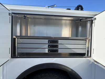 Service body storage compartment on a 2025 Mack MD7, showing four slide-out steel drawers inside a metal cargo bay with latching handles.