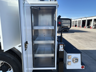 Mack MD7 service truck rear storage cabinet open showing multiple empty shelves.