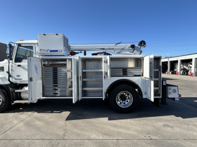 Mack MD7 service truck side view with multiple open compartments showing tool/storage lockers and hydraulic boom in the truck bed.
