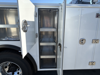 Front-side cabinet doors of a new Mack MD7 service truck showing open vertical storage compartments with multiple shelves inside a white utility body.