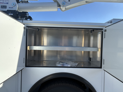 Service/utility truck bed compartment open showing empty stainless storage box with a divider shelf in a new Mack MD7 truck.