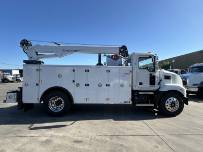 Service/utility truck with aerial bucket crane mounted on utility body, Mack MD7 cab, numerous storage compartments, and crane arm folded on top.