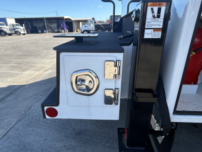 Mack MD7 service truck side view showing exterior storage compartment door with locking latch and handle, mounted on white body with black step edge.
