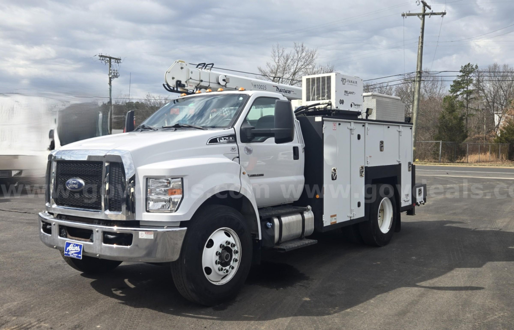 Ford F-750 service truck with utility body and crane on a dealership lot.