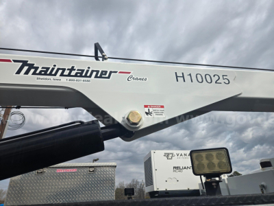 Ford F-750 service truck crane arm with Thribtrainer Cranes branding and H10025 stock number, showing hydraulic pin joint and utility equipment in background.