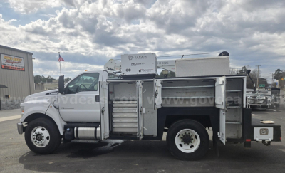 Side view of a white Ford F-750 service/utility truck with multiple compartments open, showing tool drawers and storage racks. Includes crane on bed and fuel tank.