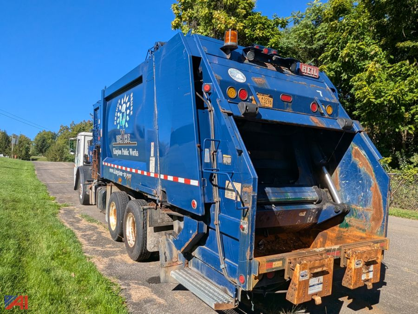 Mack Leu613 refuse truck in blue, rear view showing hopper and loading chute, side logos, safety lights, and rear bumper with rust accents.
