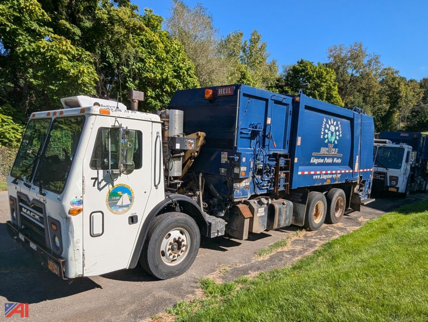White Mack Leu613 truck with blue refuse body in-service showing cab and side of rear compactor body with logo and text.