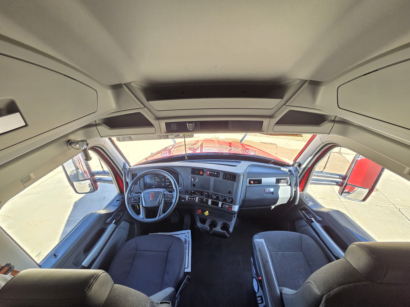 Cab interior of a 2023 Kenworth T680 truck showing driver seat, steering wheel, dashboard, and overhead console.