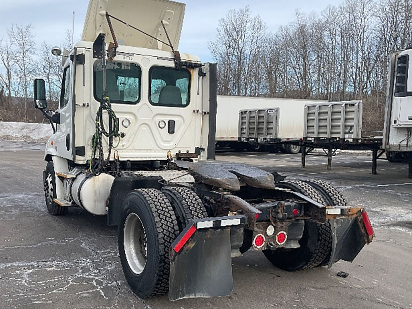 Truck rear view of a white Freightliner Cascadia daycab chassis showing fifth wheel and dual rear axles with mudflaps.