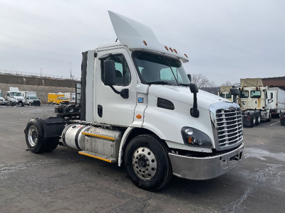 Truck cab in front view with raised hood, white Freightliner Cascadia 113 daycab tractor, fuel tanks, and chassis visible.
