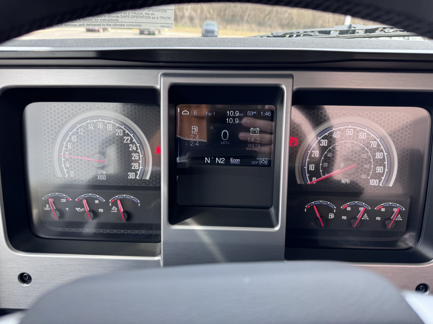 Dashboard of a 2027 Mack PI64T showing instrument cluster with speedometer and tachometer, center display screen, various gauges and warning lights.