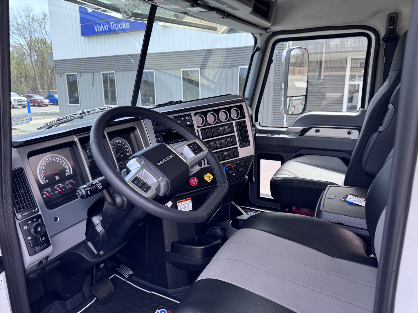 Interior of a 2027 Mack PI64T truck cab showing steering wheel, dashboard with gauges, and front seats.