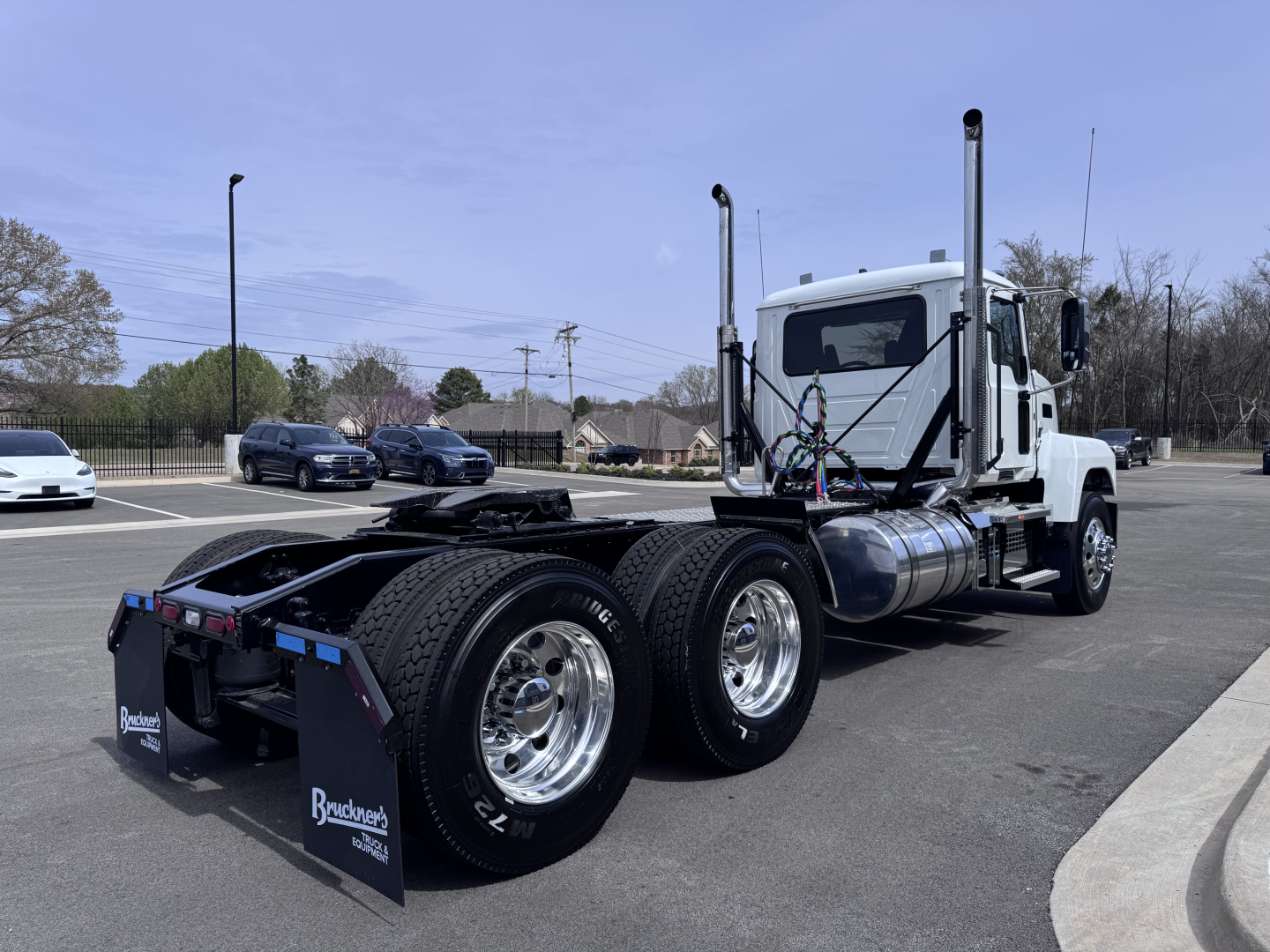 Mack PI64T conventional daycab truck with dual rear axles and chrome wheels, white cab, fuel tanks, exhaust stacks, side mirrors in a parking lot.