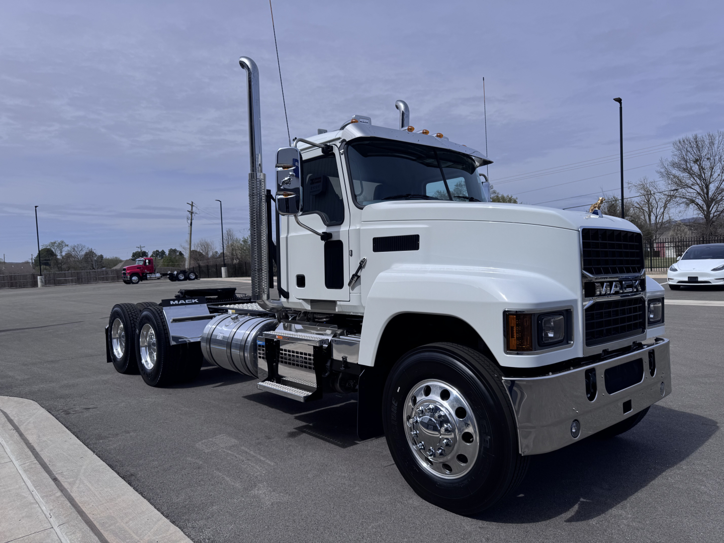 Mack PI64T truck in a parking lot seen from side, with white cab, chrome bumper, dual rear axles, fuel tanks, and exhaust stacks.