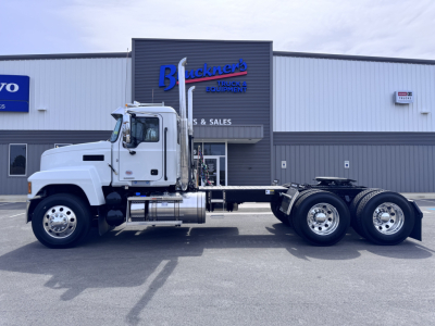 2027 Mack PI64T truck chassis side view showing cab and dual rear axles in front of a dealership.