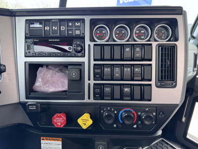 Dashboard of a new Mack PI64T truck showing instrument cluster, switches, and controls; text visible includes Mack stereo area and various gauges.