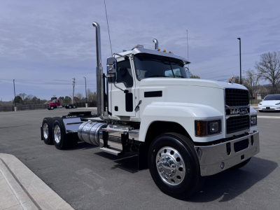 Mack PI64T truck in a parking lot seen from side, with white cab, chrome bumper, dual rear axles, fuel tanks, and exhaust stacks.