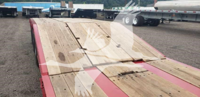 Lowboy trailer deck showing wooden planks and red-painted ramps, viewed from rear with other trailers in background.