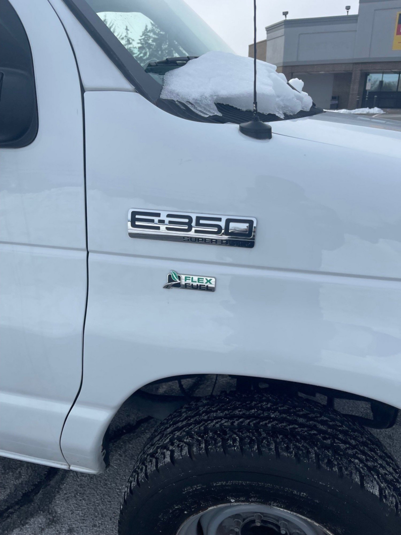Ford E-350 Super Duty cargo van side view showing E-350 badge and Flex Fuel badge on white body with snow on hood and windshield.