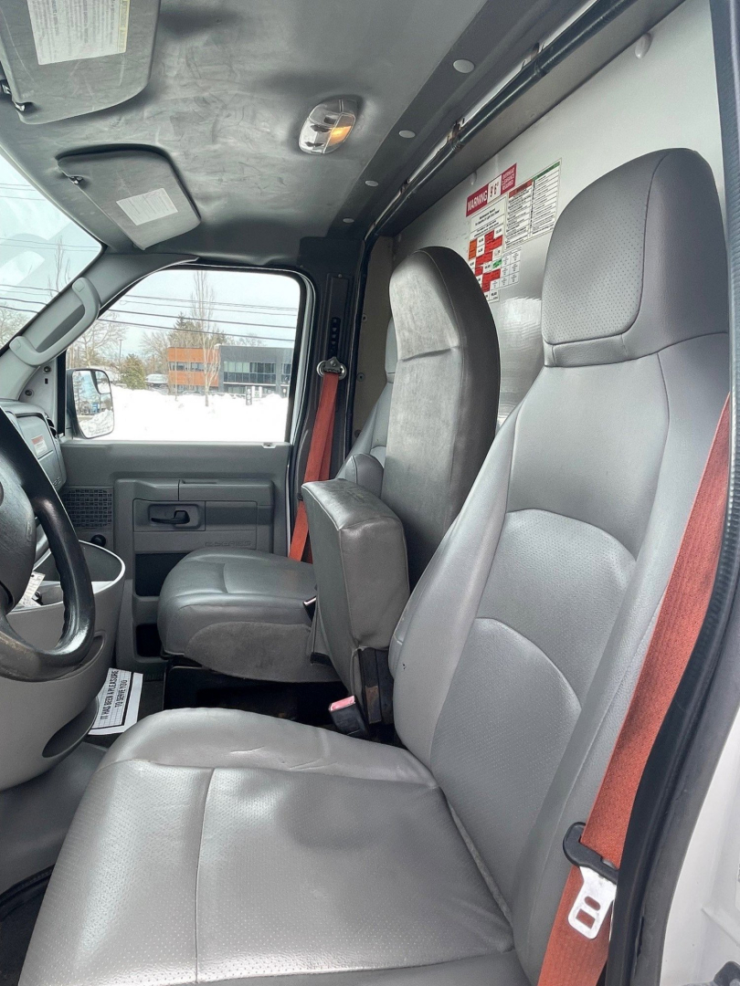 Interior of a 2014 Ford Econoline commercial cutaway truck cabin showing front seats and side door, with warning labels on the panel and a view toward the window.