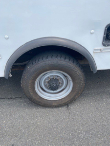 Truck wheel well and wheel of a Ford Econoline commercial box van showing steel rim and tire, partial body with light grey panel.