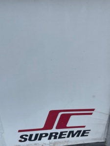 Image shows the lower corner of a vehicle with a Supreme JC logo on white body panel; no legible text about the truck specs visible.