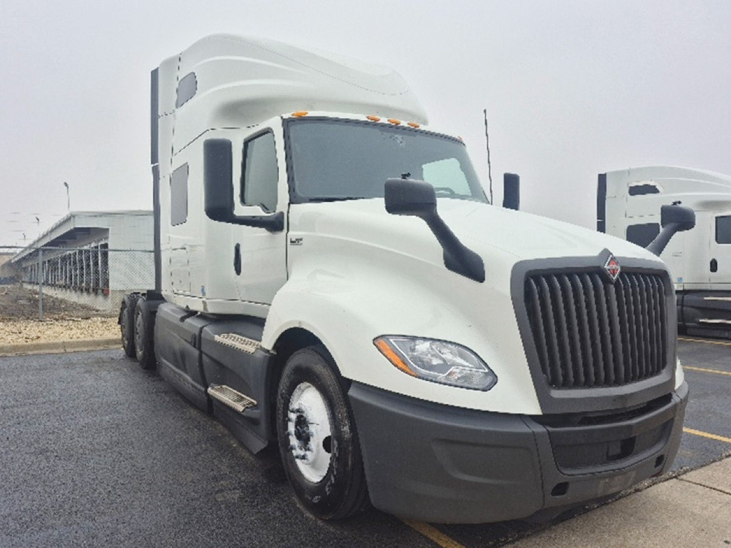 Truck with white sleeper cab showing large black grille, side mirrors, and dual rear axles. No visible text on image aside from general truck design.