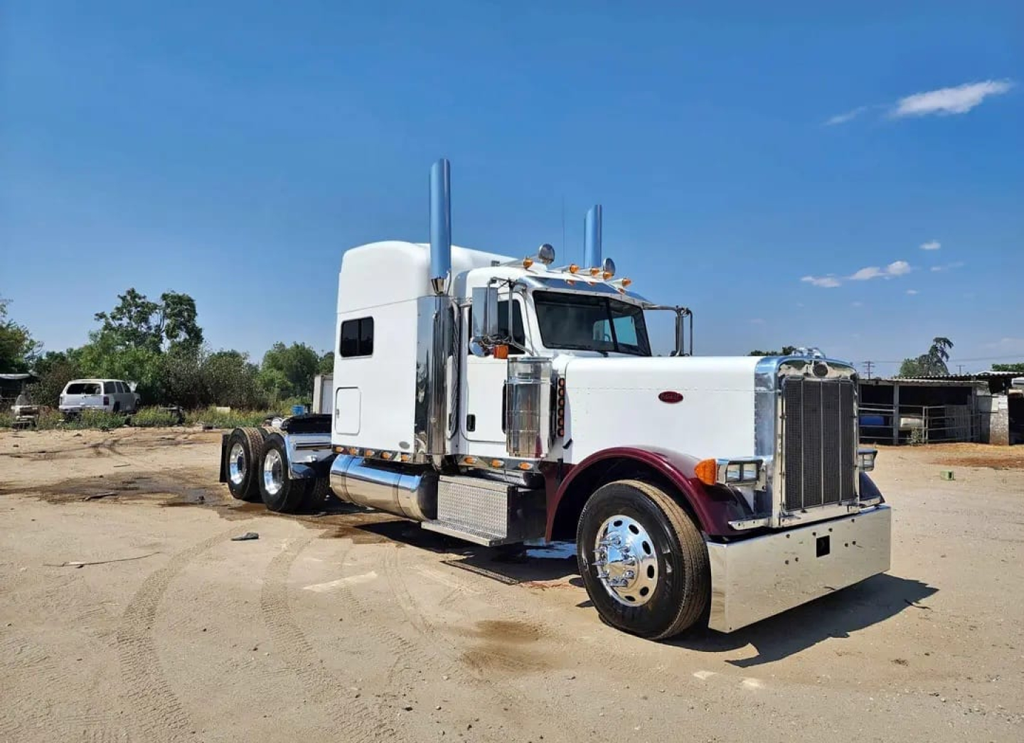 Peterbilt 379 heavy haul truck in white with chrome grille and stacked exhausts, side view showing dual rear axles and large front bumper.
