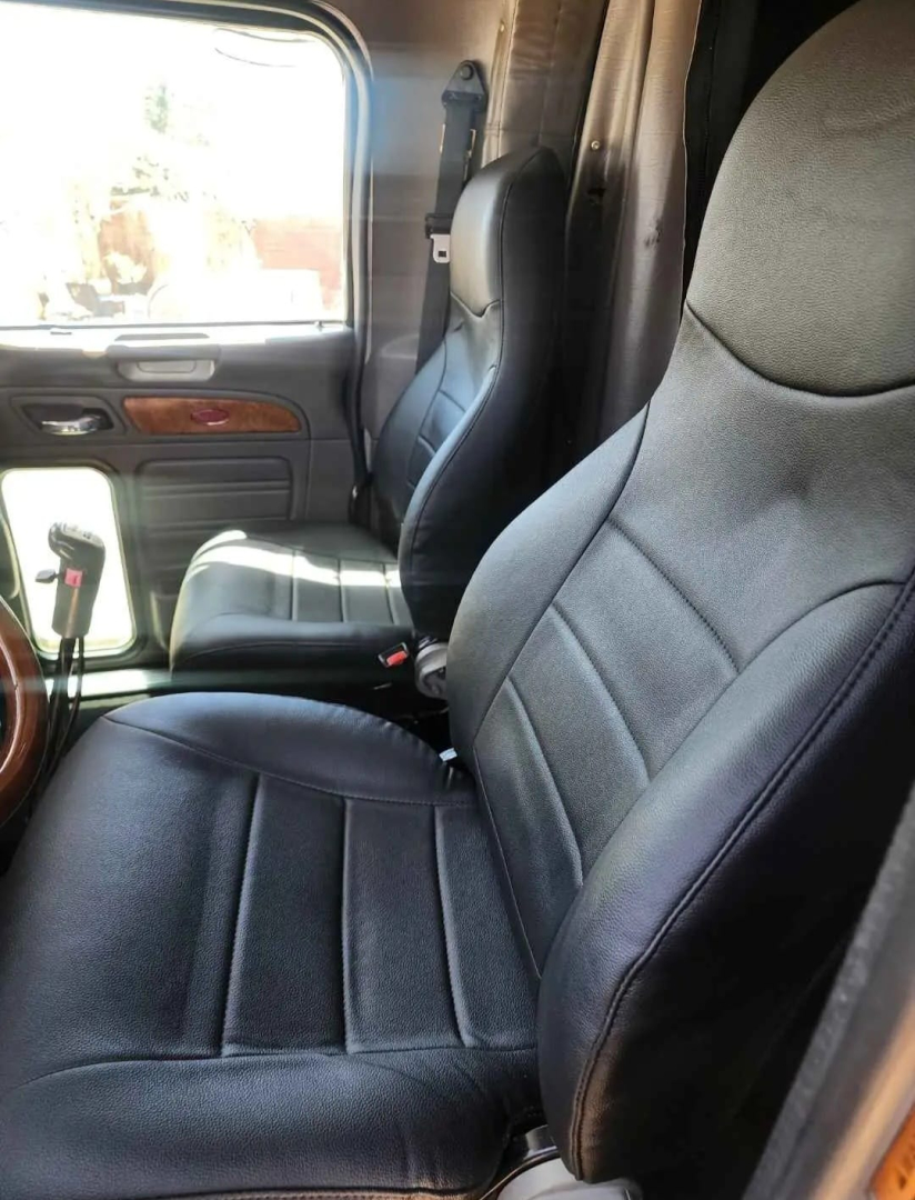 Peterbilt 379 interior seating view showing driver's seat and passenger seat with dark upholstery, door panel, and window.