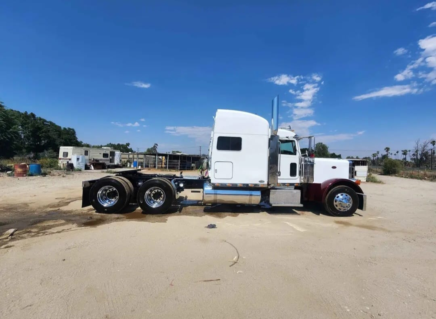 Peterbilt 379 tractor-trailer side view showing white sleeper cab, chrome fuel tanks, dual rear axles, and large exhaust stacks.