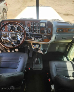 Truck cab interior showing steering wheel, dashboard with multiple gauges, center console, and gear shifter.