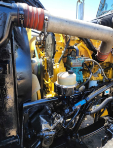Peterbilt 379 engine bay showing coolant reservoir, turbo piping, yellow engine components, and hoses.
