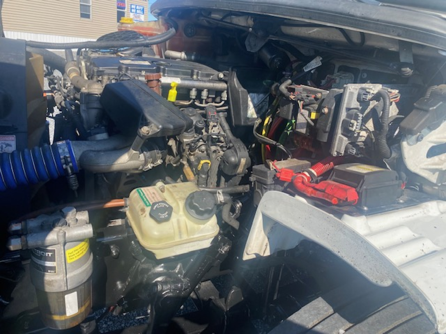 Engine bay view of a 2019 Freightliner M2 106 refrigerated truck showing coolant reservoir, battery, and various hoses