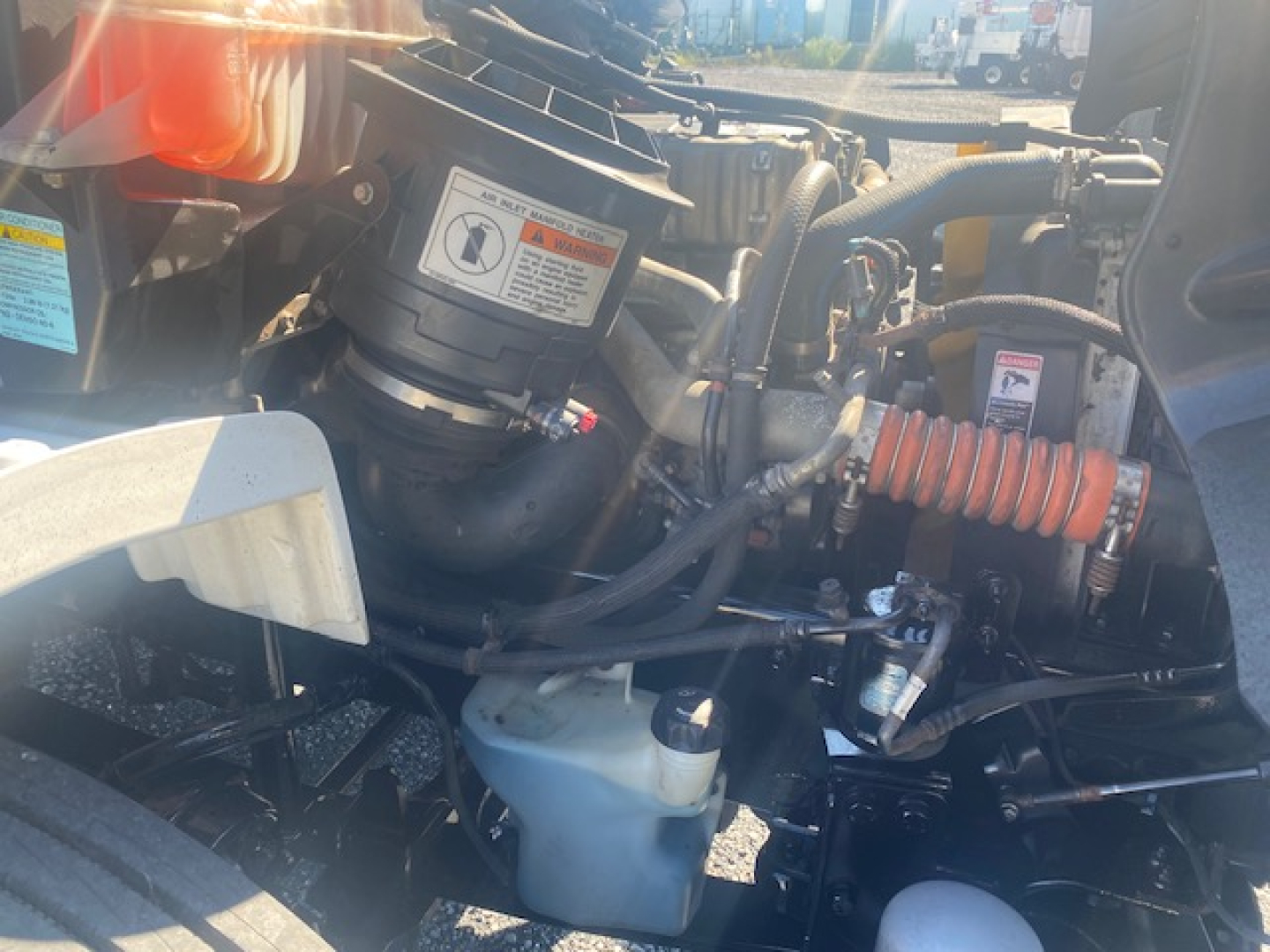 Freightliner M2 106 engine bay showing coolant reservoir, hoses, and air filter housing with labels and warning stickers.