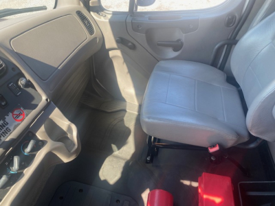 Cab interior of a Freightliner M2 106 truck showing driver and passenger seats and dash panel.