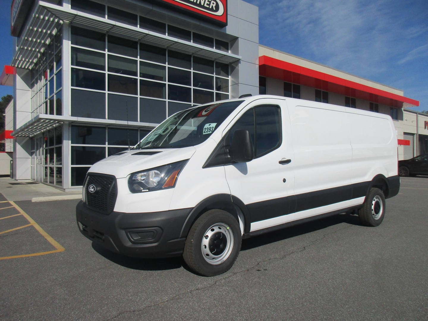 New 2026 Ford Transit cargo van parked outside dealership showing white exterior and black front grille with cargo van shape.