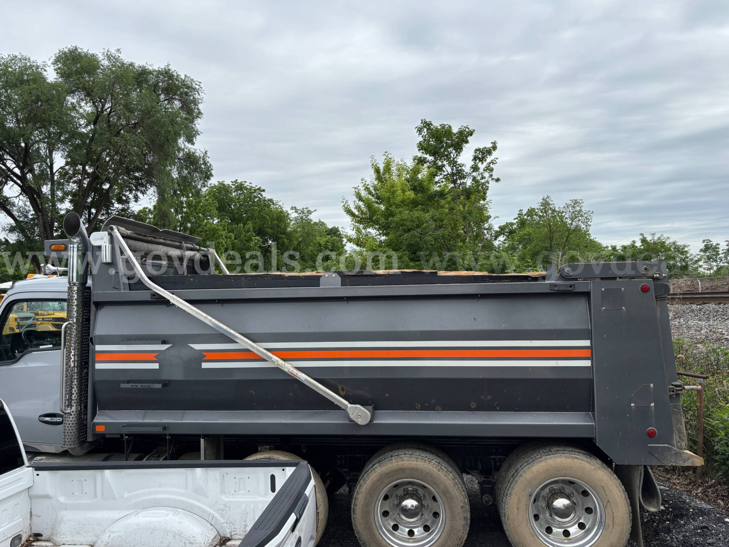 Dump truck bed of a 2021 Kenworth T880 with orange and white stripe decal and hydraulic lift arm visible; no legible text besides logos on the truck bed.