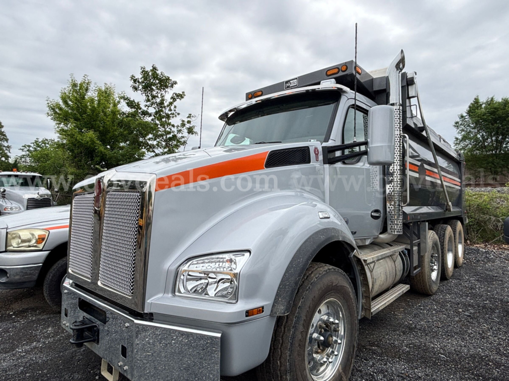 Kenworth T880 dump truck in gray with orange accents, front grille, dual rear wheels, and dump bed visible.