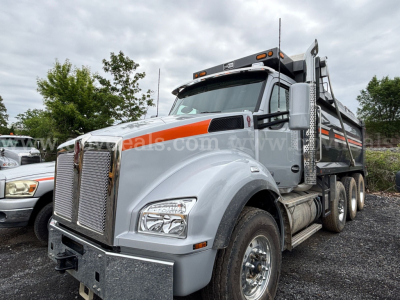 Kenworth T880 dump truck in gray with orange accents, front grille, dual rear wheels, and dump bed visible.