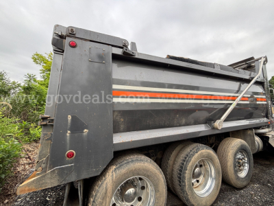 Kenworth T880 dump truck side view showing triple rear axles and striped orange/white decal along the hopper.