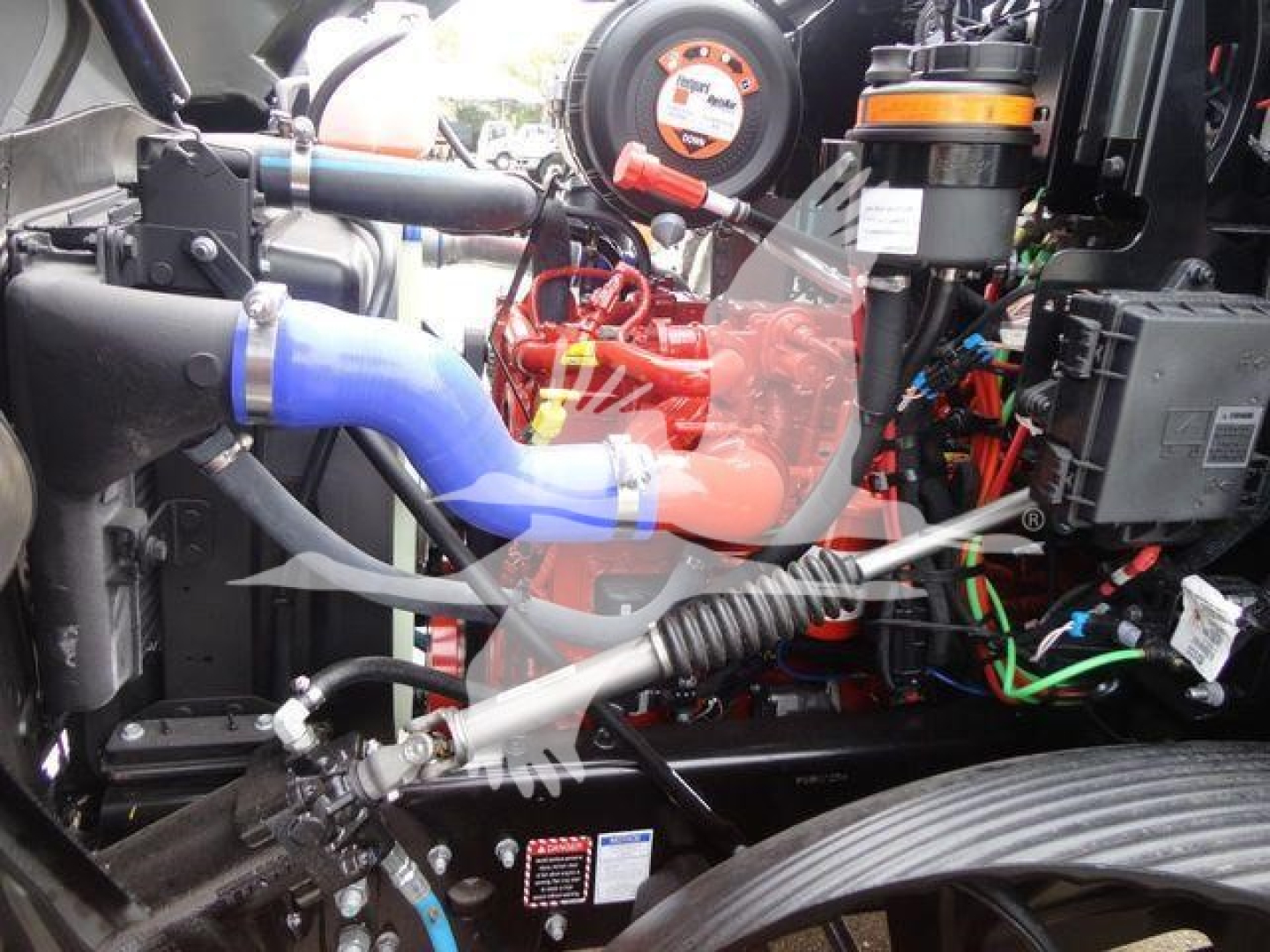 Trucked engine bay view showing blue coolant hose, red engine components, black wiring loom, and orange filters.
