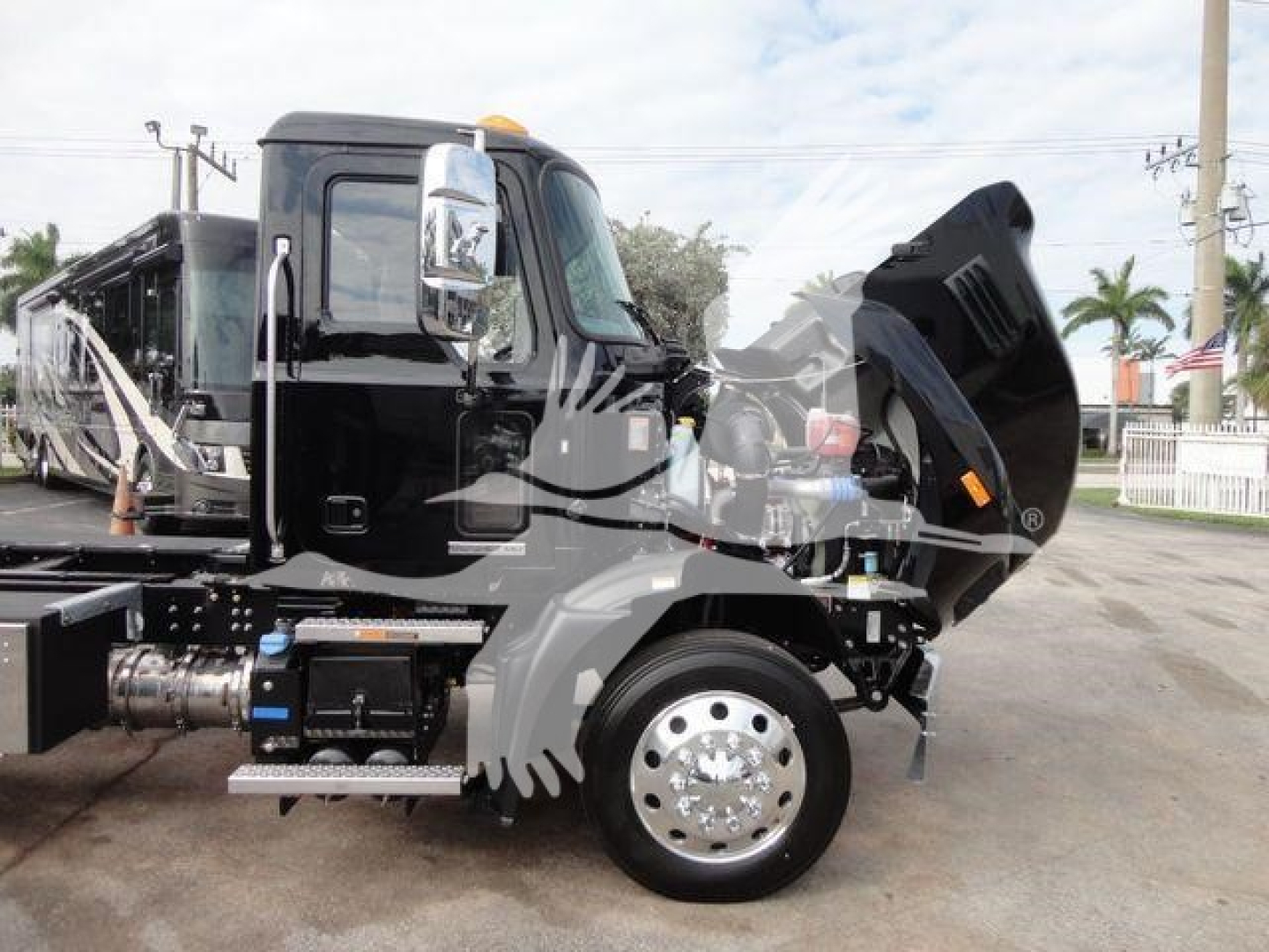 Truck hood open showing engine bay and hydraulic components on a 2027 Mack MD6 rollback truck, chrome wheel, black cab, raised hood, side step, and front fender.