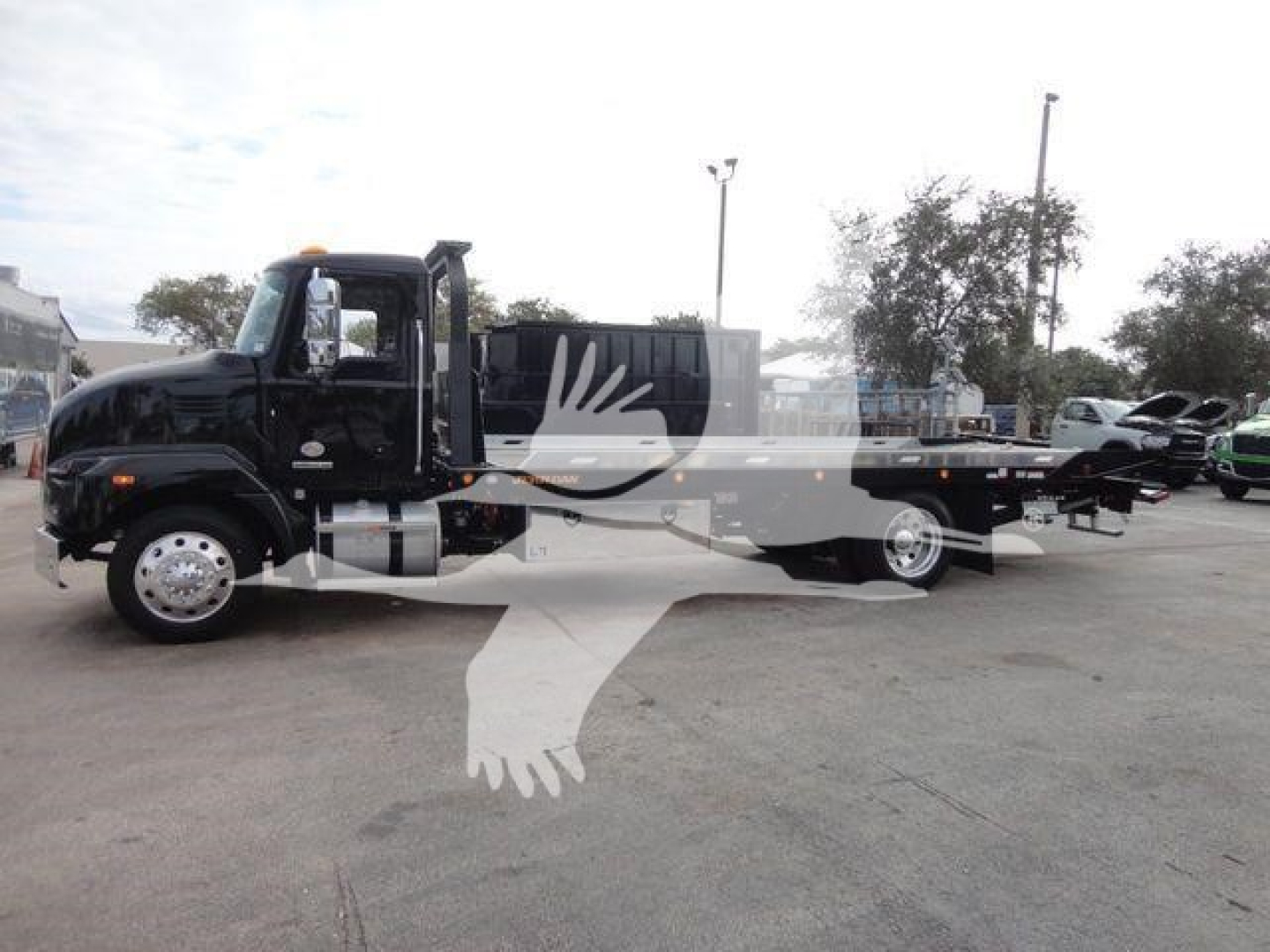 Truck bed tow/rollback body on a black 2027 Mack MD6 truck in a dealership lot.