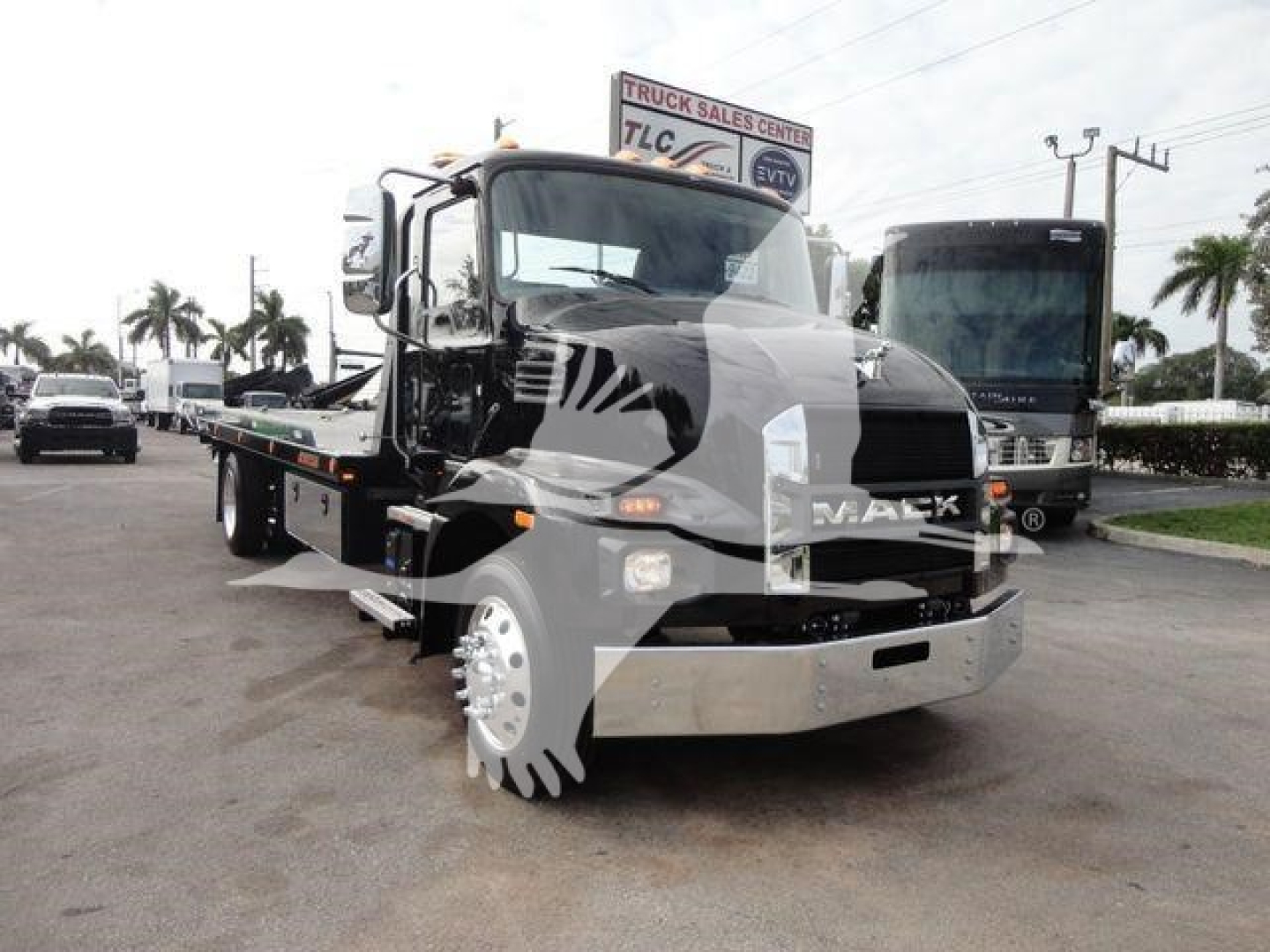 Mack MD6 rollback tow truck front view with flatbed, chrome bumper, and stock number sign in background.