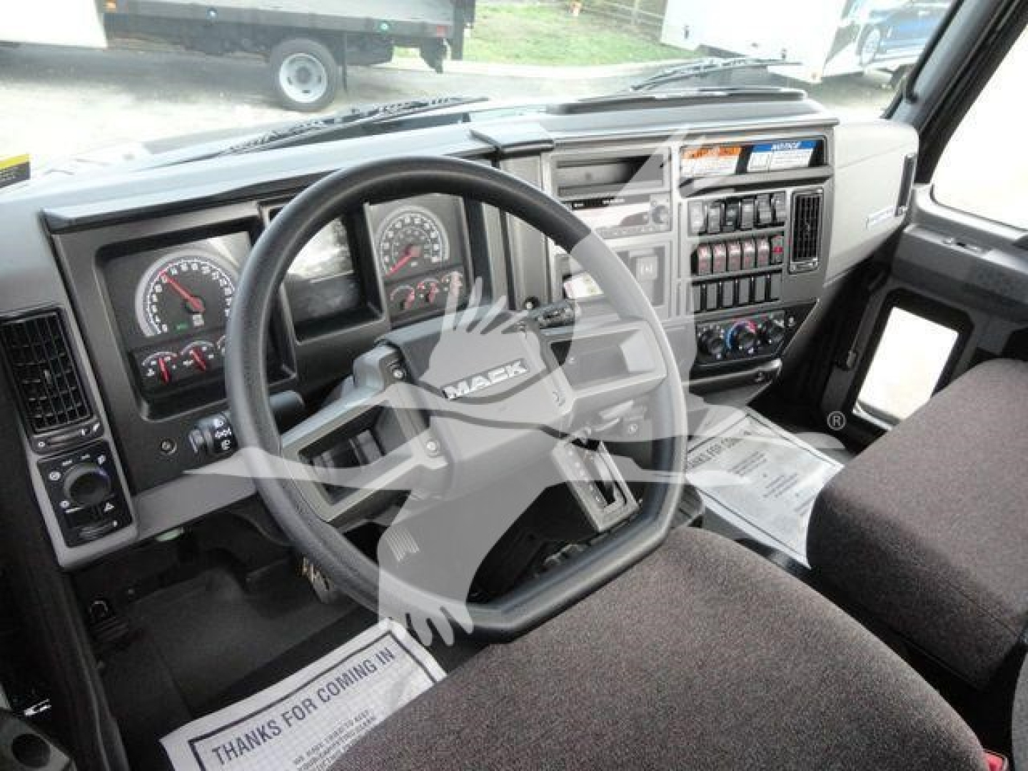 Cab interior of a Mack MD6 truck showing steering wheel, dashboard gauges, and center console with controls.