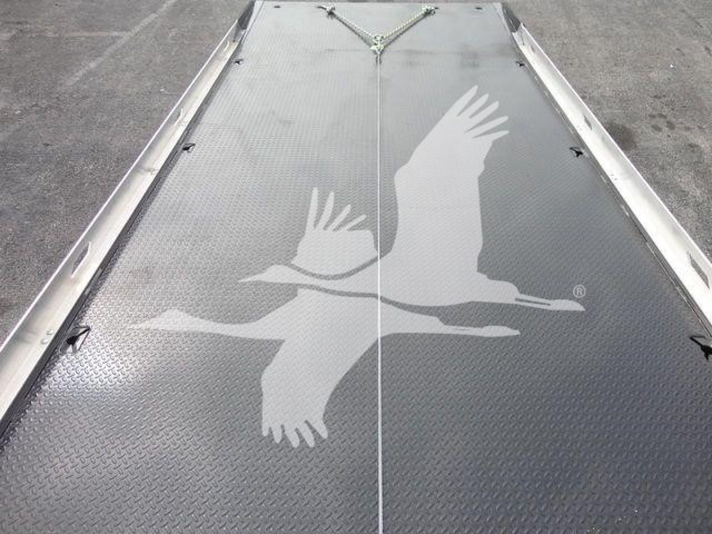 Flatbed truck deck with diamond plate surface and a large white flying gull logo in the center, seen from above.