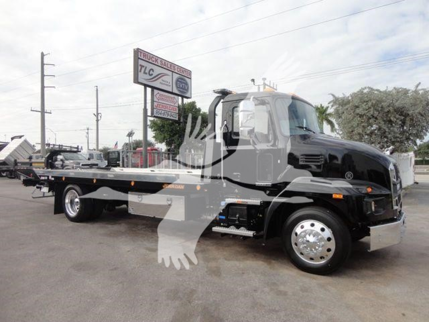 2027 Mack MD6 rollback truck with flatbed in service lot showing cab and towing bed.