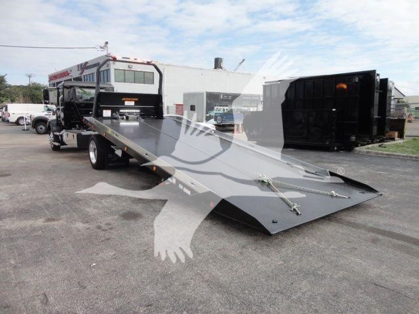 Mack MD6 rollback tow truck with lowered flatbed ramp, front cab visible in background, outdoor lot.